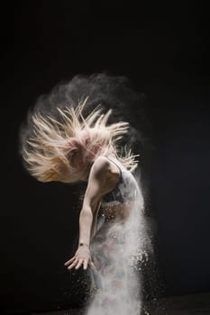 Long-haired blonde wearing top and leggings jumping in a white dust cloud profile cropped shot in dark room