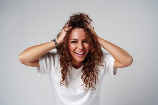 A woman in a white shirt and ripped jeans posing positively with a playful expression in a light studio setting close up