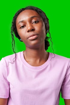 Young woman with an expression of contemplation poses against a bright green background in studio