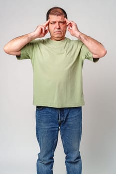 A middle-aged man experiencing stress while holding his head in hands against a neutral background close up