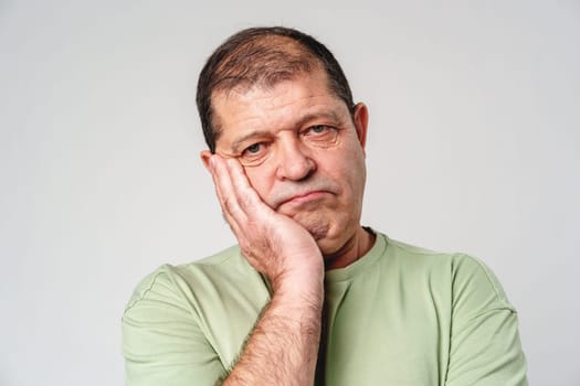 A middle-aged man shows a contemplative expression while resting his chin in his hand against a neutral background indoors