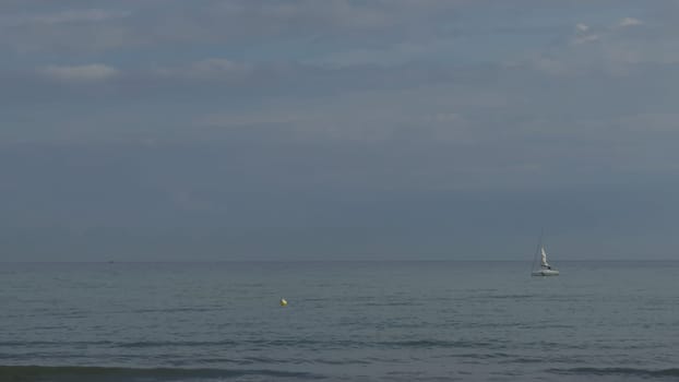 A sailboat gently moves over calm waters near a beach boundary buoy.