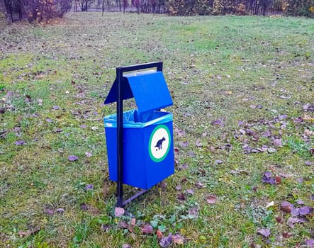 Blue dog waste bin on green grass in a park.