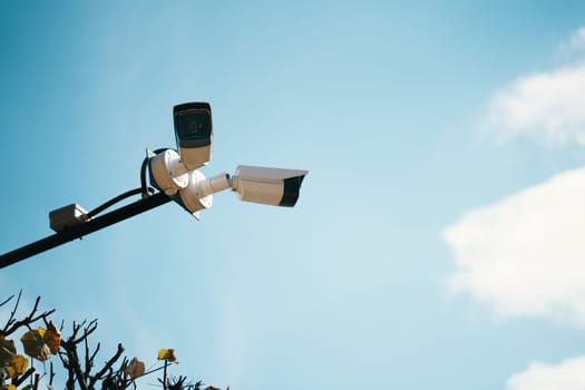 Two surveillance cameras are mounted high on a pole, meticulously observing their surroundings under a bright blue sky