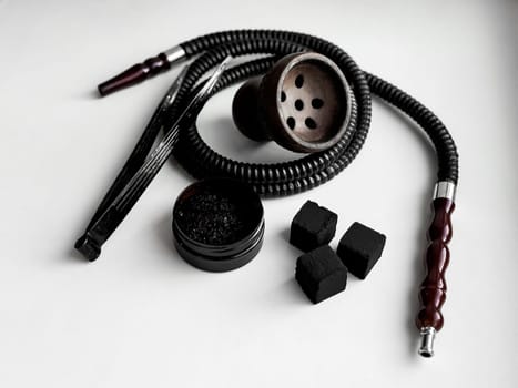 Traditional hookah set with hose, bowl, tongs, and charcoal on white background.