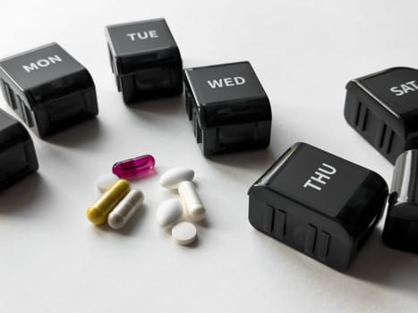 Weekly pill organizer with multicolored capsules and tablets for daily medication management.