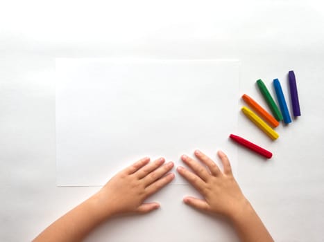 Childs hands preparing to draw with colorful crayons on white paper.
