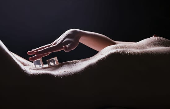 Ice cubes lying on naked woman body cropped view in dark room