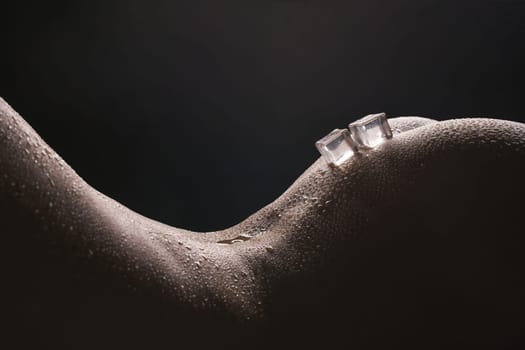 Ice cubes lying on naked woman body cropped shot in dark room