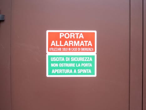 Cremona, Lombardy, Italy October 15th 2024 Close up of an alarm and emergency exit sign providing safety instructions in italian on a brown metal door