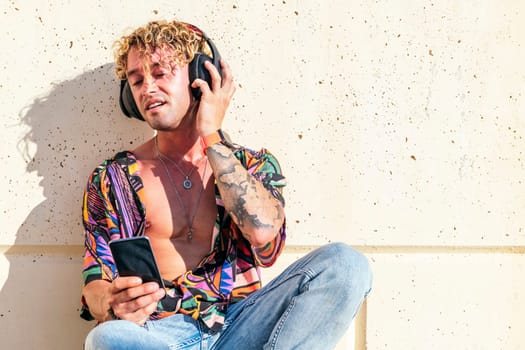 male hipster sitting on street and enjoying songs in headphones with closed eyes