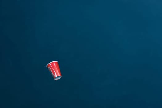 Red paper cup from Coca-Cola floats in a blue sea. Top view. High quality photo