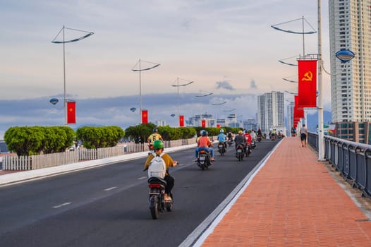 Motorbike traffic on road on a bridge with Vietnam flags in a city in Asia in summer. Nha Trang, Vietnam - August 22, 2024