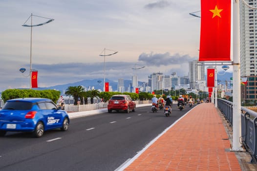 The traffic of motorbikes and cars on the road on the bridge with the flags of Vietnam in Asia. Nha Trang, Vietnam - August 22, 2024