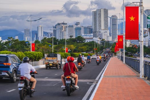 Motorbike traffic on the road on a bridge with Vietnam flags in a city in Asia during rush hour. Nha Trang, Vietnam - August 22, 2024