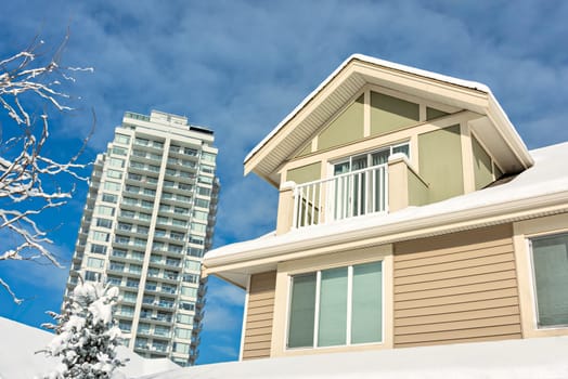 Top of residential house in snow and high-rise building on cloudy sky background.