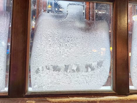 Frost collects on window glass, creating a delicate frost pattern as light shines from inside