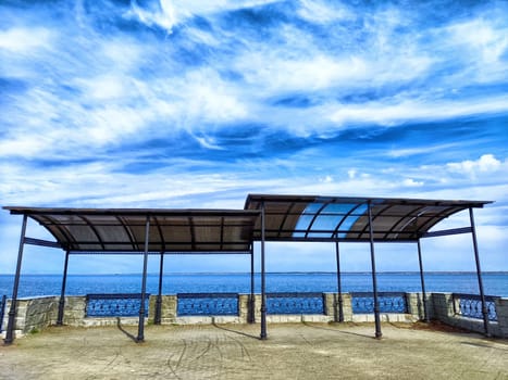 An empty, covered patio overlooking a calm, blue sea on sunny day