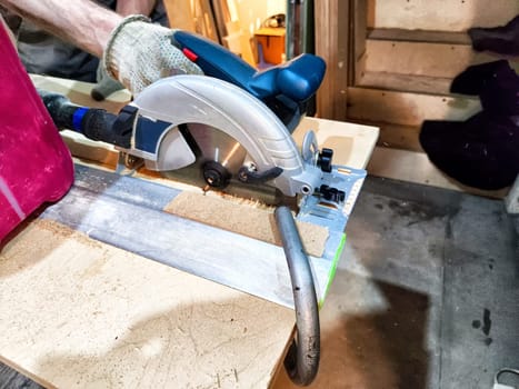 Close-up of a person cutting a piece of wood with circular saw in a workshop
