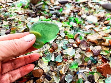 green glass pebble in hand on the beach with colored pebbles in Glassy Bay in Vladivostok