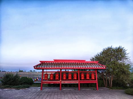 Kalmykia, Russia - April 22, 2024: Prayer drums stand peacefully under a traditional shelter at the temple of the Golden Buddha, framed by a tranquil twilight in Elista.