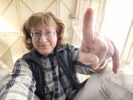While waiting at the airport, a middle-aged woman enjoys herself by taking a playful selfie, capturing her excitement and the lively atmosphere around her.