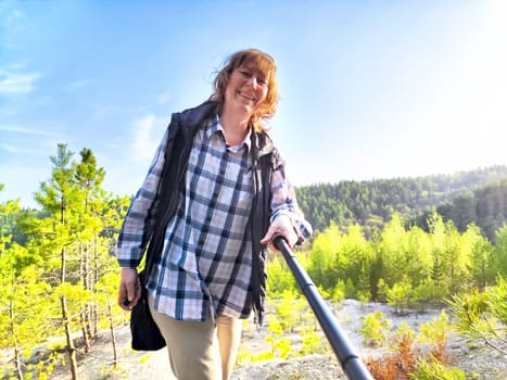 Happy female blonde tourist taking selfie picture with smart mobile phone outside. Middle aged woman having fun on adventure nature trip in mountains