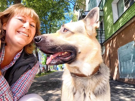 A woman is cheerfully posing for a picture alongside a friendly German Shepherd dog, capturing a joyful moment together in the frame