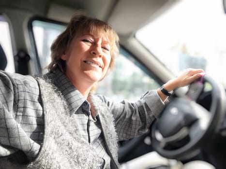 A middle-aged woman beams with happiness as she navigates through the city streets in her car, enjoying her journey.