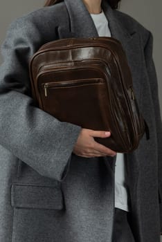 woman posing with a leather backpack wearing a warm gray coat .
