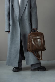 woman posing with a leather backpack wearing a warm gray coat and black boots.