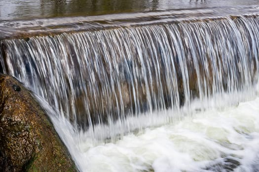 Cascade waterfall in a local reservoir. Close-up of flowing water over a concrete weir in a river