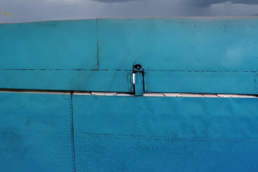 Part of an airplane wing painted blue, viewed from below.