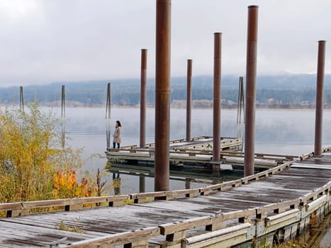 A landscape photo of a woman standing on a dock looking out at the calm water of the Pend Oreille River in eastern Washington.