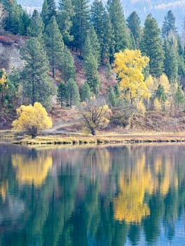 A seasonal landscape photo of fall colors from the trees reflecting off the calm Pend Oreille River in eastern Washington.