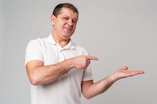 Man dressed in a white polo shirt and jeans happily pointing to the side against a plain background close up