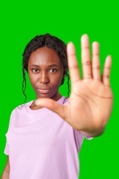 A young woman in a lilac shirt holds her hand up against a bright green background close up