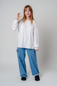 Casual young woman posing confidently in a white shirt and blue pants against a neutral background indoors