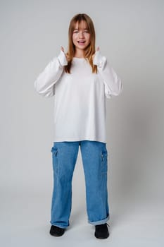 Young girl with long hair showing thumbs up against a plain background during a cheerful indoor moment