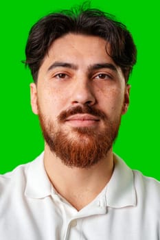 A smiling young man with a beard poses against a bright green background close up