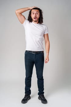 A man with curly hair expresses surprise while looking upwards in a neutral background close up