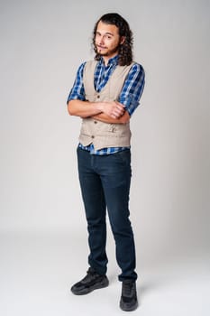 A confident young man with curly hair poses against a neutral backdrop indoors