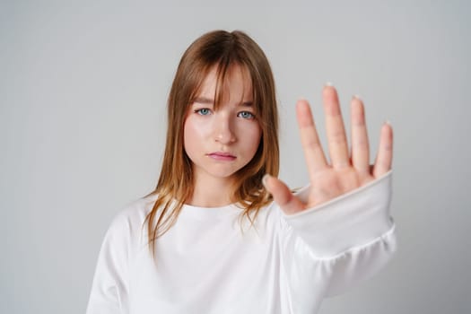 Young woman with long hair holding up her hand against a plain background close up