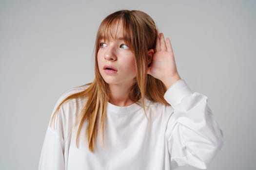 Teen girl with straight hair demonstrates listening pose against a plain background in a casual setting