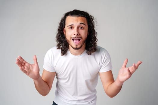 Young man with curly hair expresses surprise in a light-colored setting close up