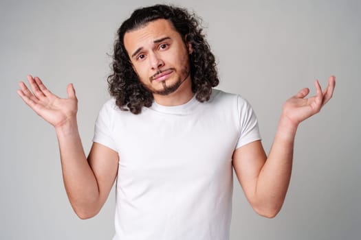A man with curly hair expressing uncertainty while standing against a neutral background during the day