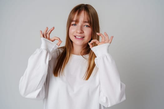 Young woman smiling and making an okay gesture in a bright, minimalistic indoor setting