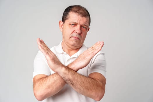 A man making a gesture of refusal with arms crossed against a light background in studio
