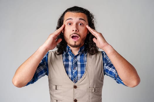 Young man with curly hair expresses surprise in a light-colored setting close up