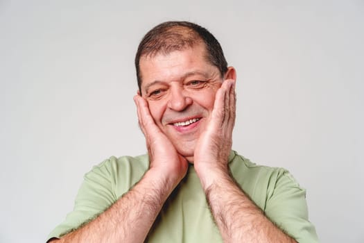 Happy middle-aged man showing joy while touching his face against a neutral background close up
